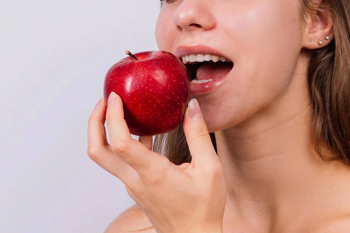 Close-up of a woman biting into a red apple, showing porcelain veneers