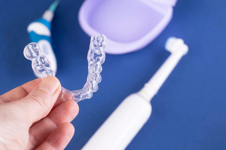 Hand holding a clear Invisalign aligner tray beside a toothbrush and storage case
